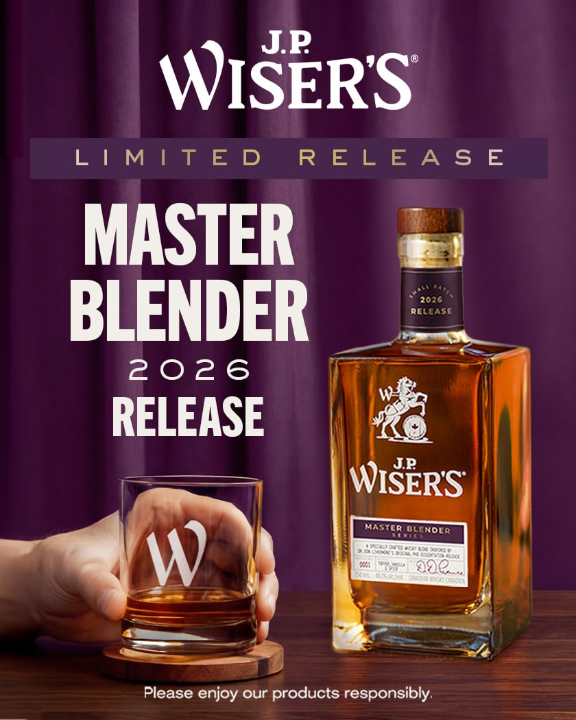 J.P. Wiser’s Master Blender 2026 Limited Release Canadian whisky bottle with wooden cap beside a glass of whisky on a wooden table